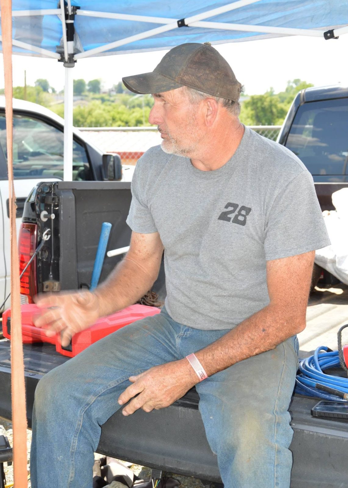 Robbie Mabe in a #28 shirt sitting on a truck tailgate in the pits